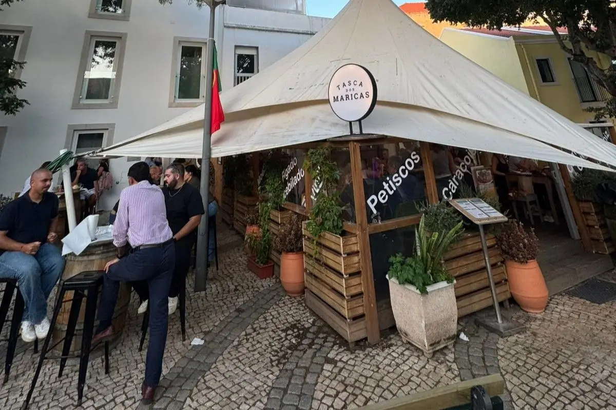 Fachada e esplanada da Tasca dos Maricas na Praça 5 de Outubro, com clientes ao balcão exterior.
