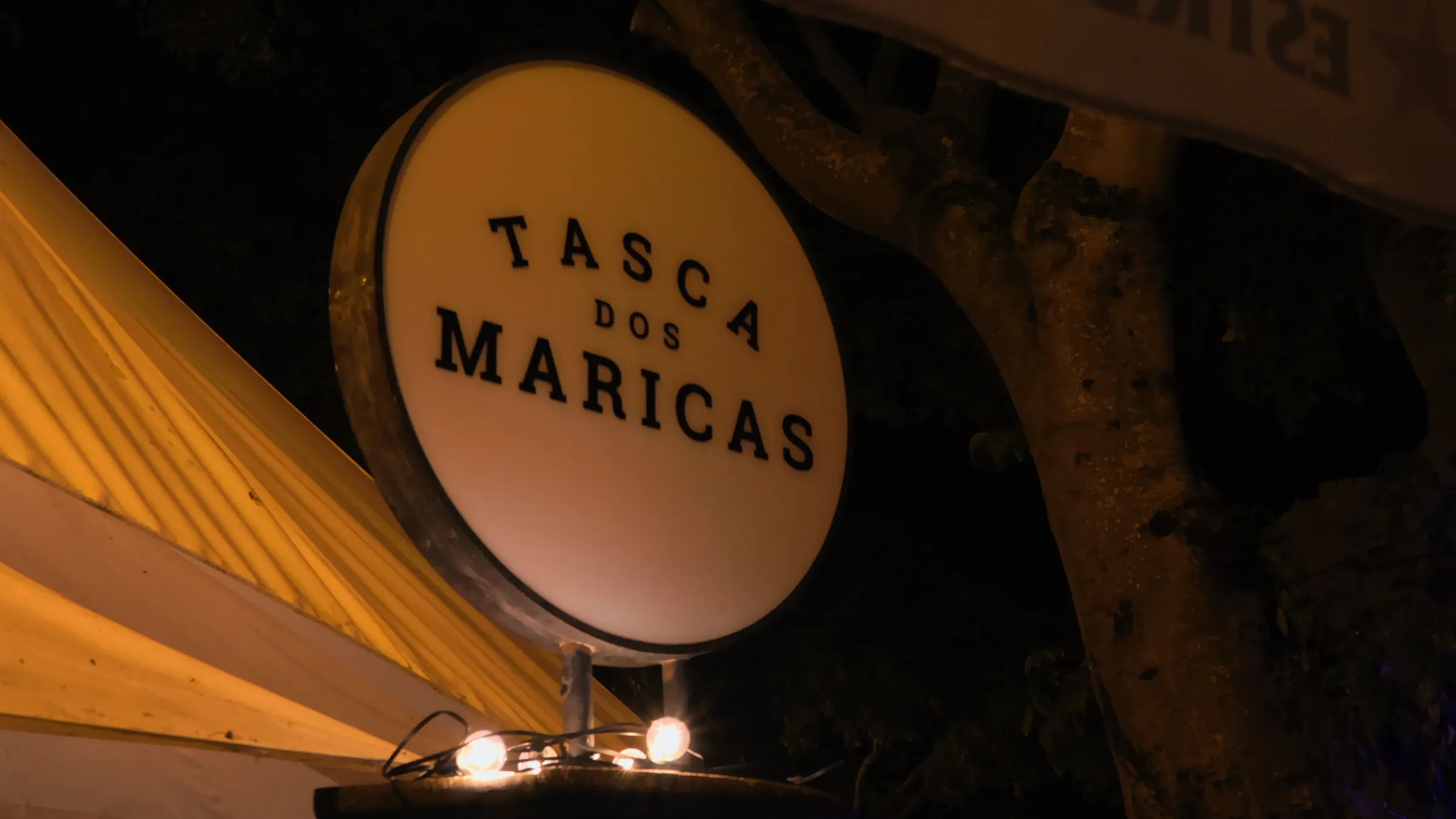 Letreiro redondo iluminado da Tasca dos Maricas, à noite.